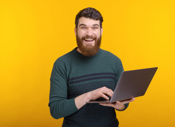 homem de suéter verde sorri enquanto segura um laptop para cancelar apostas online de costas para um fundo amarelo