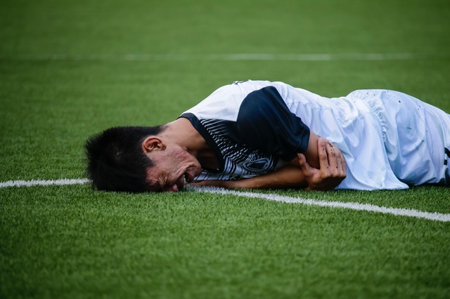 jogador asiático deitado em campo chorando com o rosto encostado na grama